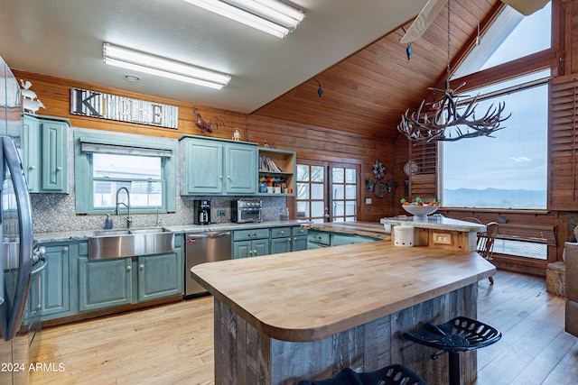 kitchen featuring stainless steel dishwasher, lofted ceiling, wood walls, and a healthy amount of sunlight