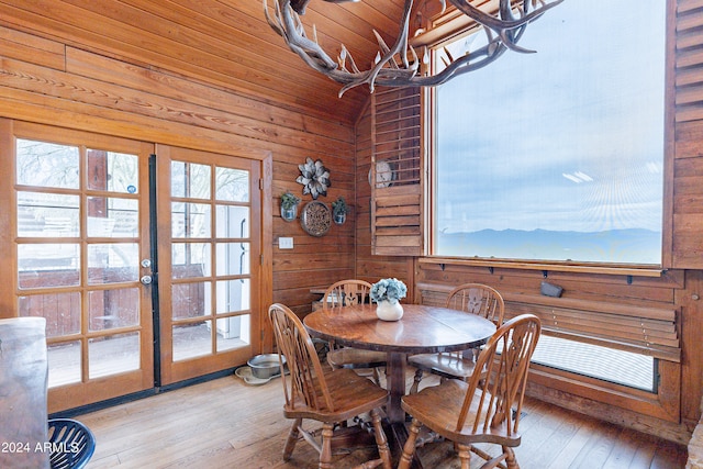 dining space featuring wooden ceiling, light hardwood / wood-style flooring, a chandelier, vaulted ceiling, and wooden walls