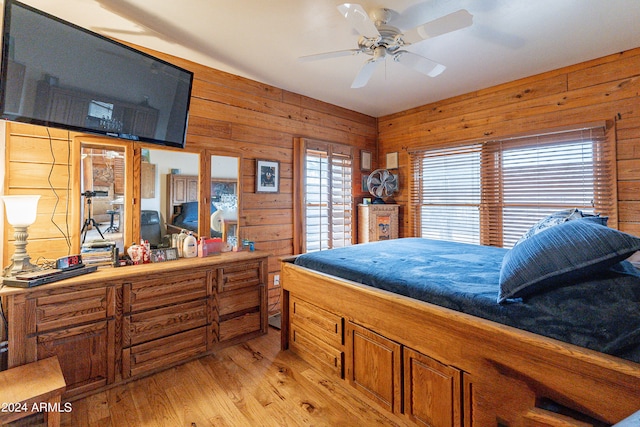 bedroom with light wood-type flooring, ceiling fan, and wood walls