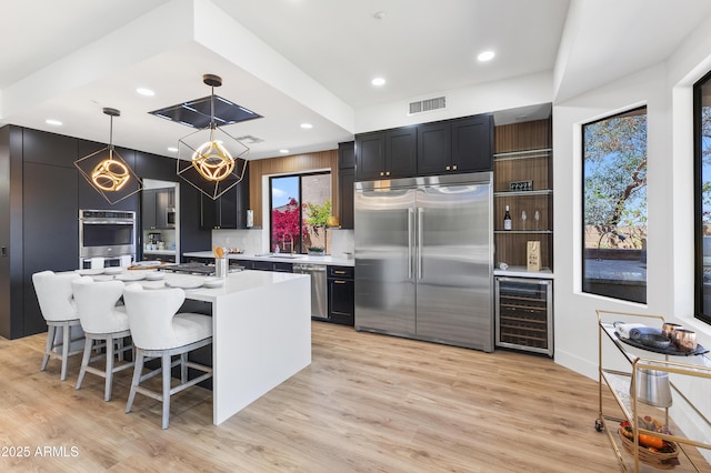 10646 E Butherus Dr, Scottsdale, AZ 85255 - kitchen with stainless steel appliances, wine cooler, light countertops, a breakfast bar area, and light wood-type flooring