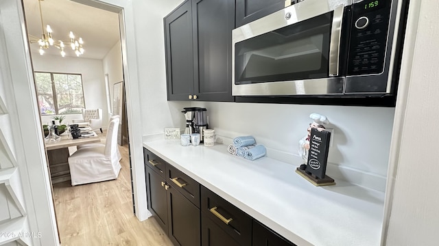 10646 E Butherus Dr, Scottsdale, AZ 85255 - kitchen with stainless steel microwave, light countertops, light wood finished floors, a chandelier, and dark cabinetry