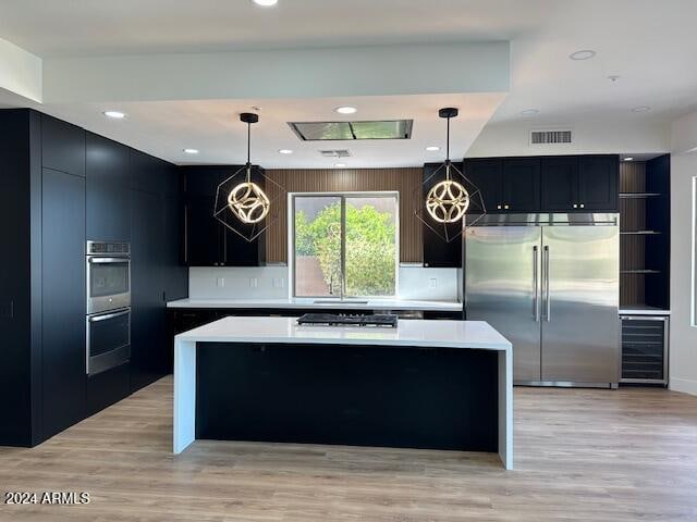 kitchen featuring pendant lighting, a center island, wine cooler, light wood-type flooring, and stainless steel appliances