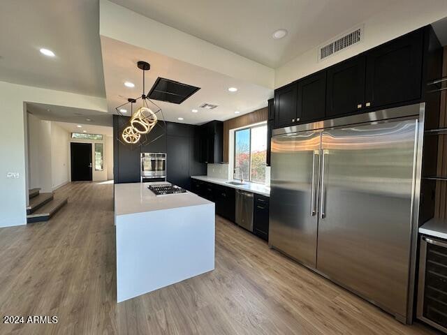 kitchen featuring wine cooler, hanging light fixtures, appliances with stainless steel finishes, and light hardwood / wood-style flooring