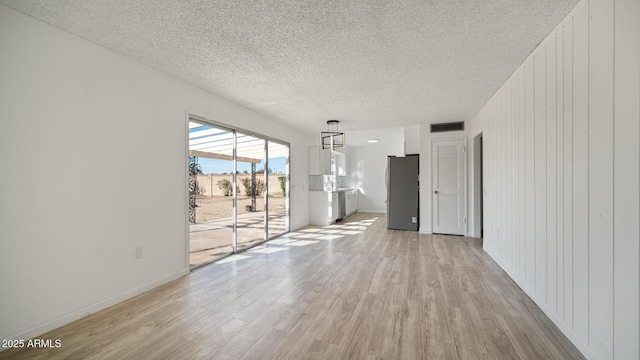 empty room with wood walls, a textured ceiling, and light wood-type flooring