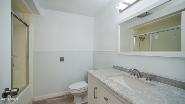 full bathroom with hardwood / wood-style floors, vanity, enclosed tub / shower combo, and toilet