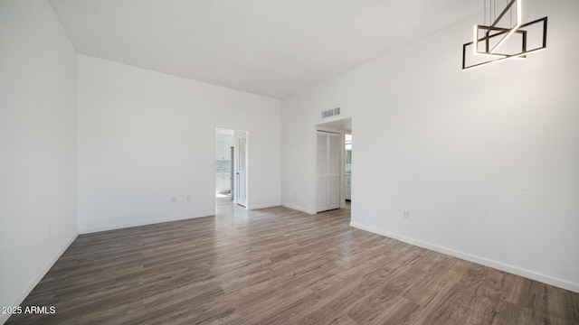 empty room with a high ceiling, dark hardwood / wood-style floors, and an inviting chandelier