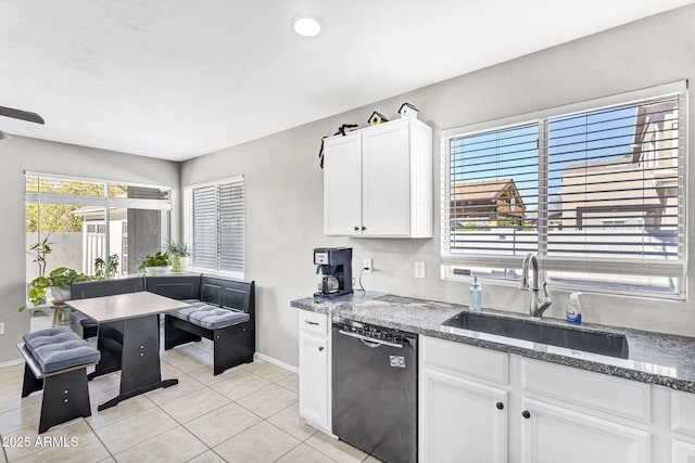 kitchen with light tile patterned floors, white cabinets, a sink, dishwasher, and baseboards