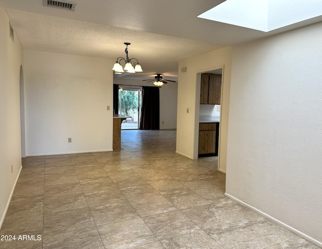 empty room with a textured ceiling, a skylight, and ceiling fan with notable chandelier