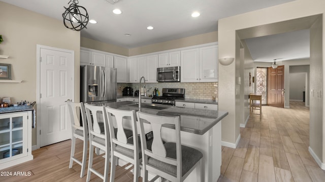 kitchen featuring appliances with stainless steel finishes, light wood-type flooring, white cabinetry, pendant lighting, and a breakfast bar