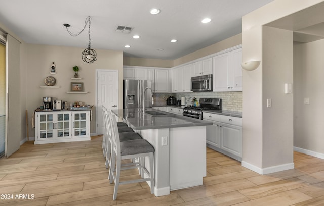 kitchen featuring appliances with stainless steel finishes, light hardwood / wood-style flooring, white cabinetry, and an island with sink