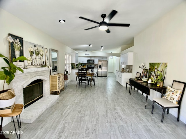 living area with light wood-type flooring, a brick fireplace, ceiling fan, and lofted ceiling