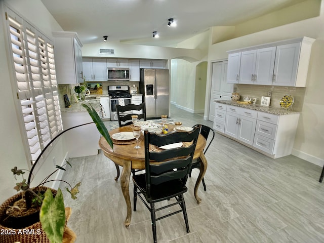 dining area featuring baseboards, arched walkways, lofted ceiling, and visible vents