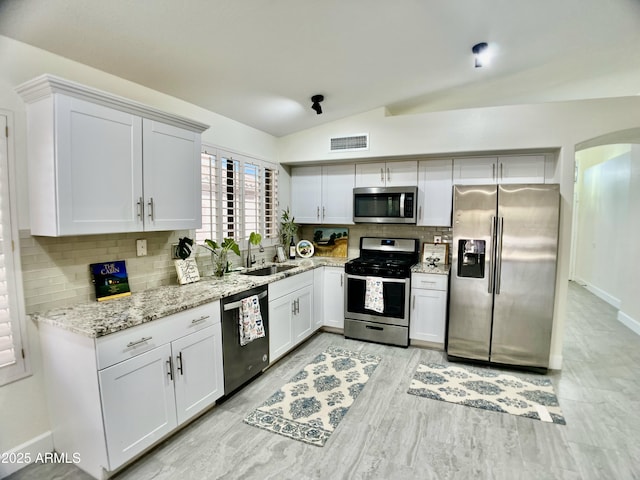 kitchen with a sink, stainless steel appliances, lofted ceiling, backsplash, and visible vents