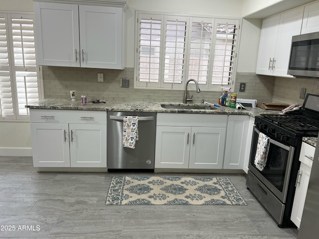 kitchen featuring backsplash, a sink, light stone counters, stainless steel appliances, and white cabinetry