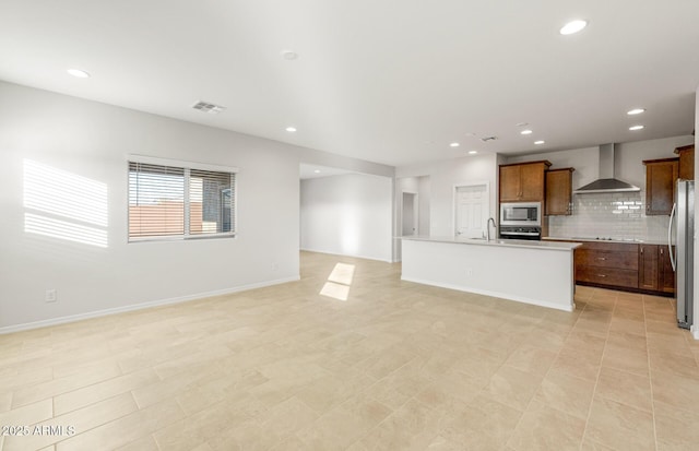 kitchen with wall chimney range hood, sink, appliances with stainless steel finishes, a center island with sink, and decorative backsplash