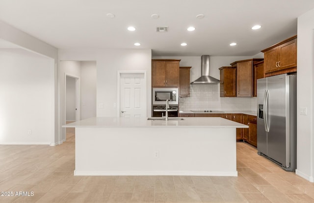 kitchen featuring sink, decorative backsplash, wall chimney range hood, stainless steel appliances, and a center island with sink