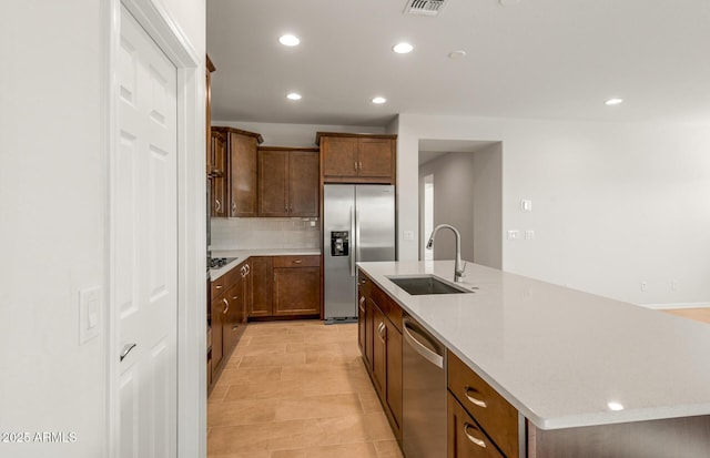 kitchen featuring an island with sink, sink, backsplash, light stone counters, and stainless steel appliances