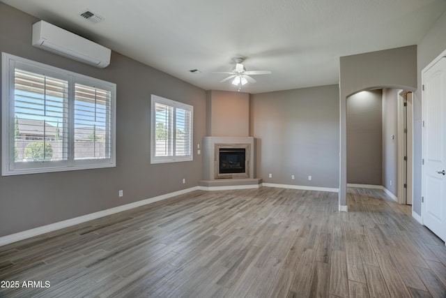 5552 N Kerwood Loop, Prescott Valley, AZ 86314 - unfurnished living room with a ceiling fan, a wall unit AC, wood finished floors, arched walkways, and a fireplace with raised hearth
