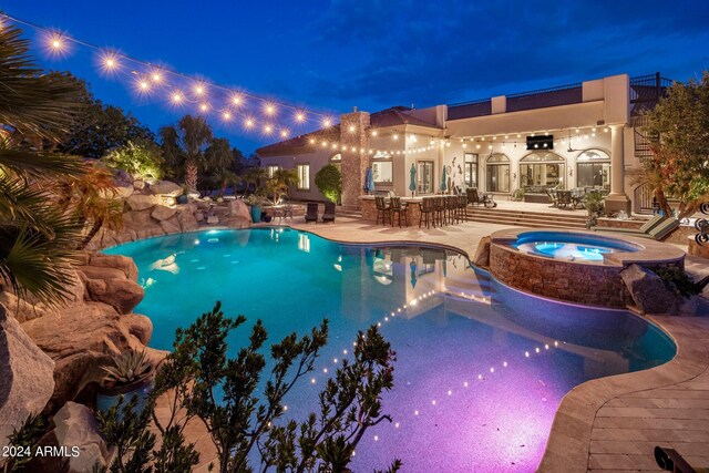 pool at night featuring an in ground hot tub and a patio area