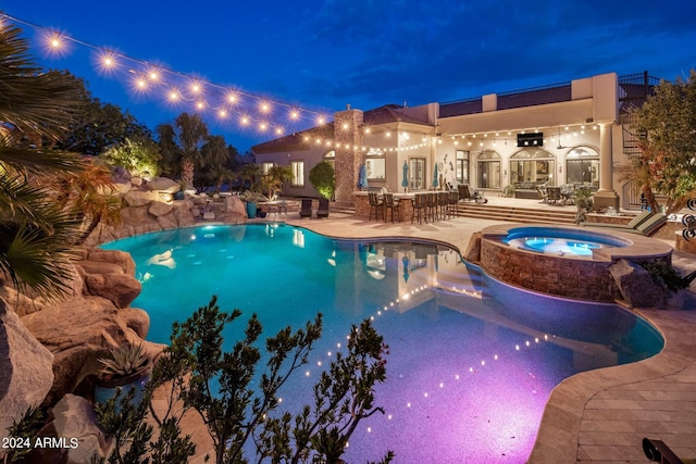 pool at twilight featuring a pool with connected hot tub and a patio