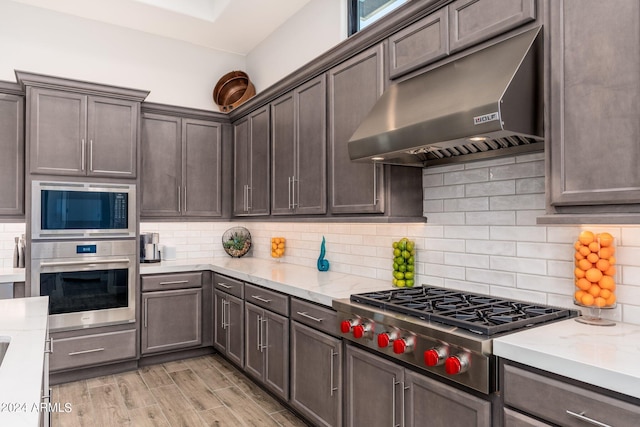 kitchen featuring backsplash, stainless steel appliances, light stone countertops, and light wood-type flooring