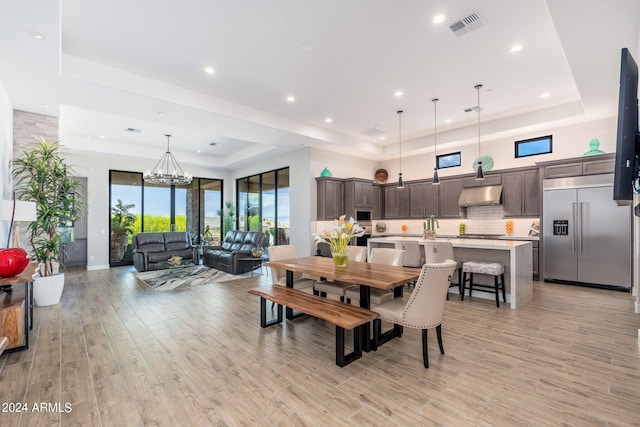 dining space with a raised ceiling, an inviting chandelier, and light hardwood / wood-style flooring