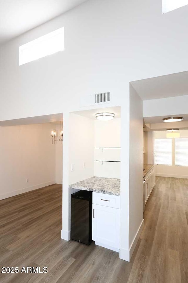kitchen featuring light wood-style floors, a chandelier, beverage cooler, baseboards, and white cabinets