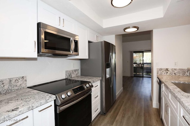 kitchen with appliances with stainless steel finishes, a tray ceiling, white cabinetry, and dark wood-type flooring