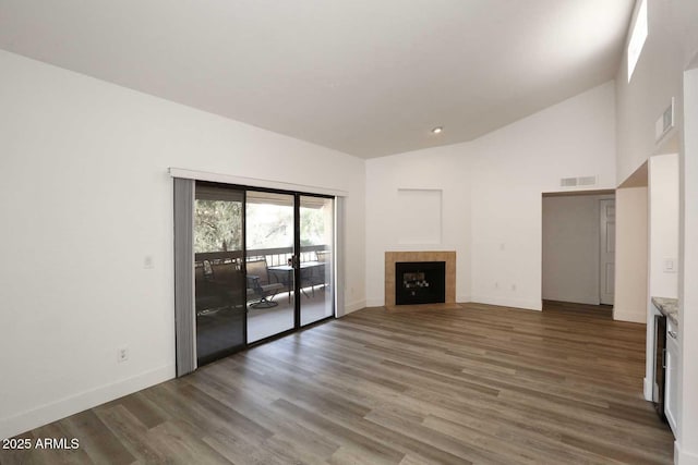unfurnished living room featuring a tile fireplace, wood finished floors, baseboards, and high vaulted ceiling