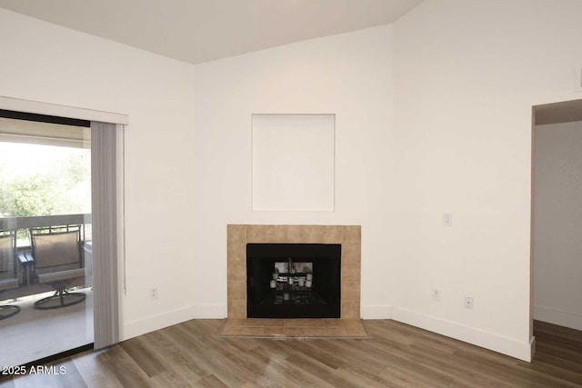 unfurnished living room featuring wood finished floors, baseboards, a tiled fireplace, and vaulted ceiling