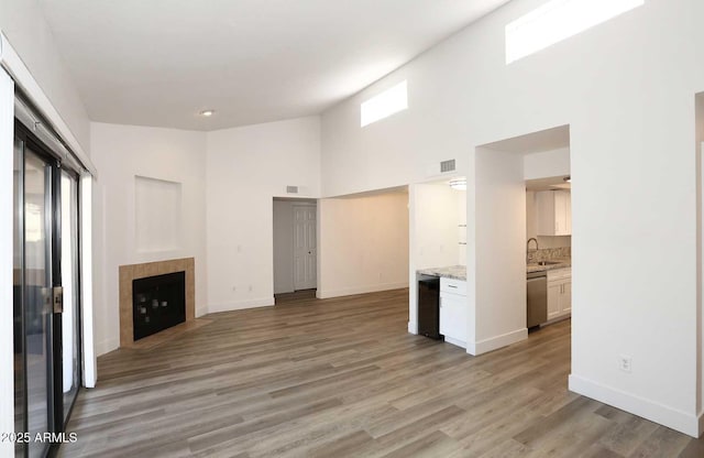 unfurnished living room featuring a tiled fireplace, a high ceiling, a sink, light wood finished floors, and baseboards