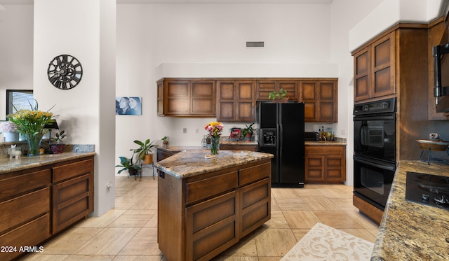 kitchen featuring light tile floors, a towering ceiling, black appliances, stone counters, and a center island