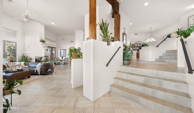 stairway featuring a high ceiling, light tile floors, and ceiling fan with notable chandelier