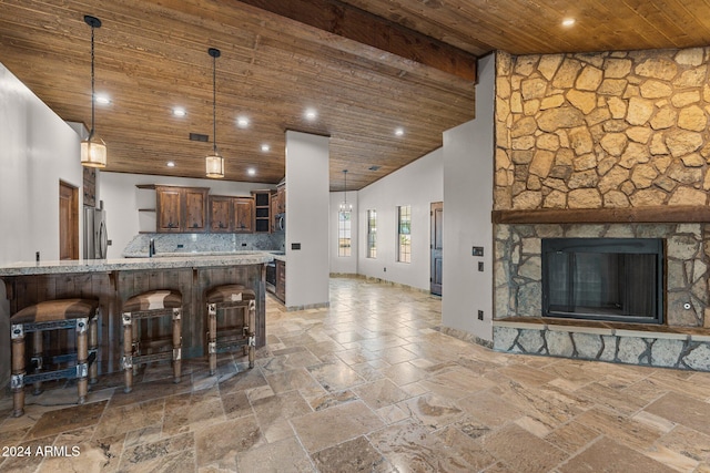 kitchen with high vaulted ceiling, stainless steel refrigerator, a kitchen breakfast bar, stone tile floors, and wood ceiling