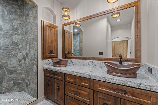 bathroom featuring a sink, tiled shower, and double vanity