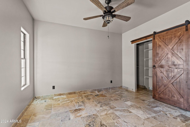 unfurnished bedroom with stone tile flooring, a barn door, a closet, baseboards, and ceiling fan