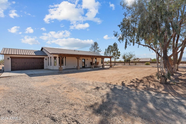 back of house with fence, driveway, an attached garage, stucco siding, and metal roof