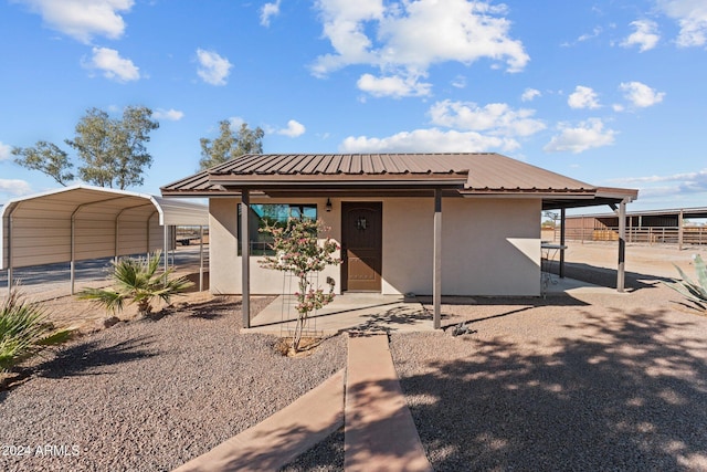 view of front of house with stucco siding, metal roof, a detached carport, and fence