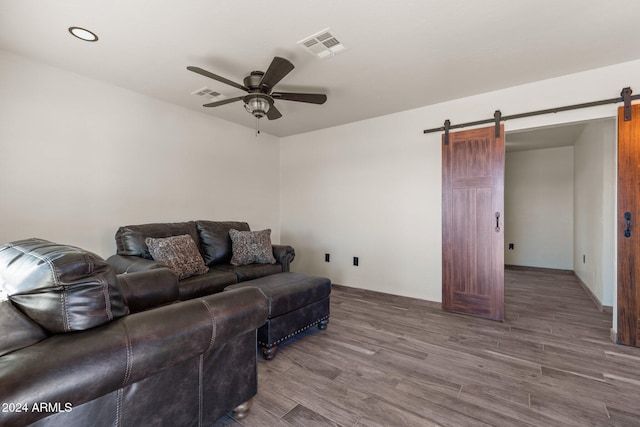 living area with a barn door, wood finished floors, visible vents, and ceiling fan