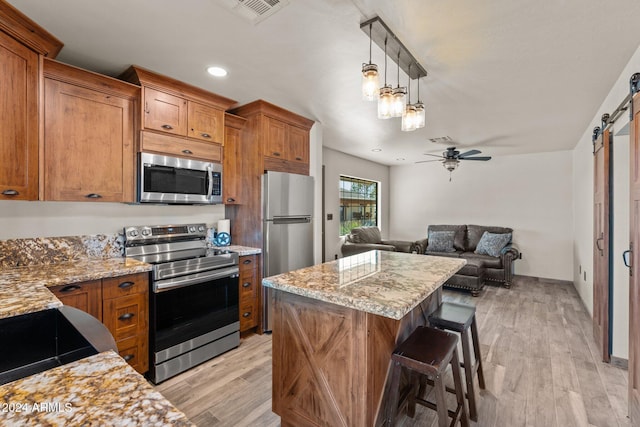 kitchen featuring stainless steel appliances, light wood-style floors, a barn door, brown cabinets, and a center island