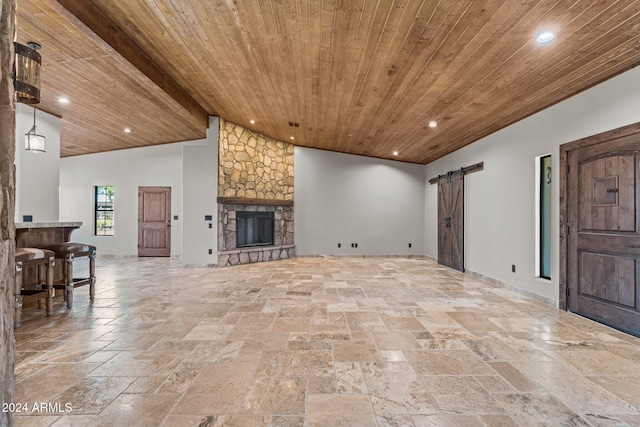 living area with wood ceiling, a barn door, a stone fireplace, recessed lighting, and stone tile flooring