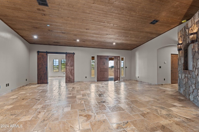 empty room featuring a barn door, wood ceiling, stone tile flooring, and visible vents