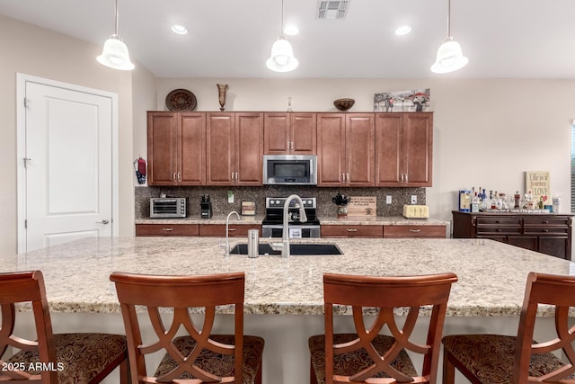 kitchen with a breakfast bar, sink, decorative light fixtures, appliances with stainless steel finishes, and an island with sink