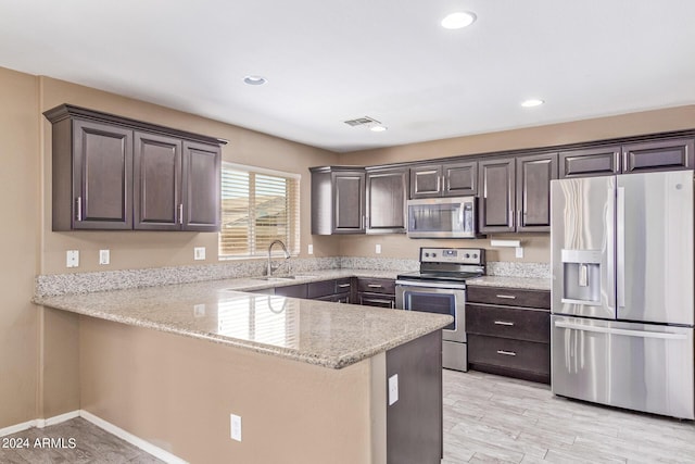 kitchen with kitchen peninsula, light stone counters, dark brown cabinets, stainless steel appliances, and sink