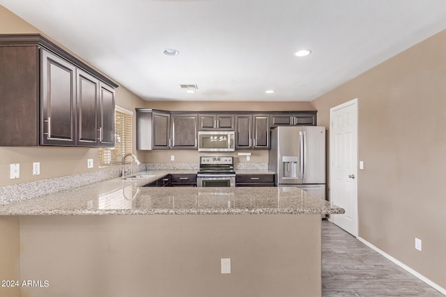 kitchen with sink, appliances with stainless steel finishes, dark brown cabinets, light stone counters, and kitchen peninsula