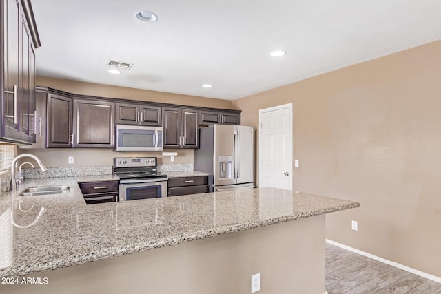 kitchen with kitchen peninsula, appliances with stainless steel finishes, light stone counters, and sink