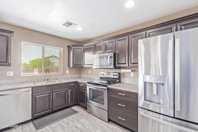 kitchen featuring appliances with stainless steel finishes, light wood-type flooring, light stone counters, dark brown cabinets, and sink