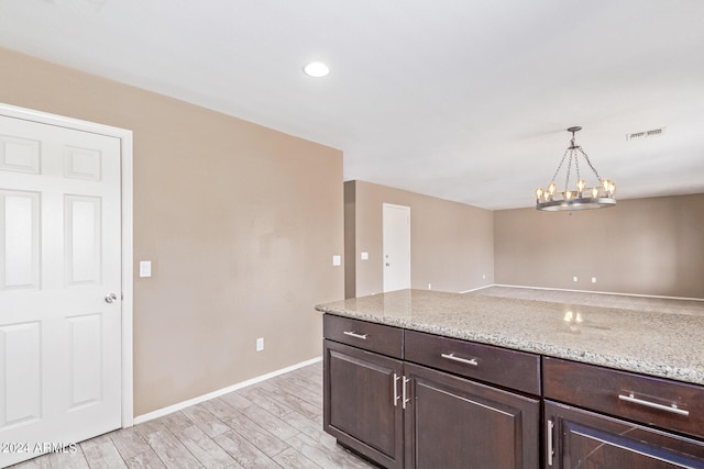 kitchen with an inviting chandelier, hanging light fixtures, light stone countertops, dark brown cabinets, and light hardwood / wood-style floors