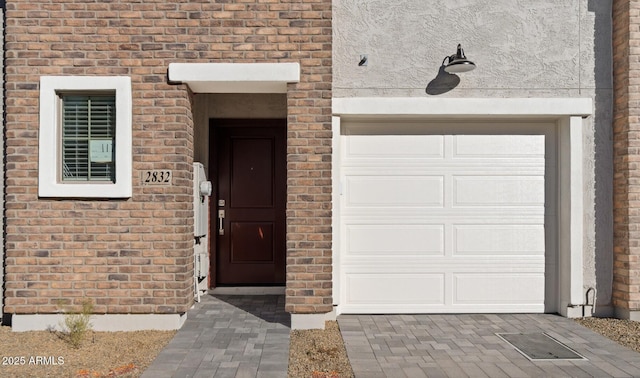 view of exterior entry with an attached garage and brick siding