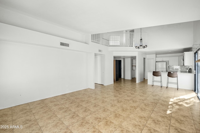 unfurnished living room featuring light tile patterned flooring, a towering ceiling, and a chandelier